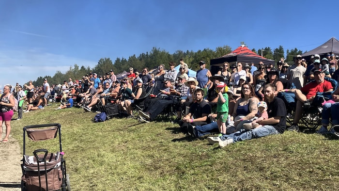 Une foule, avec des gens assis et debout, sur une butte de gazon.