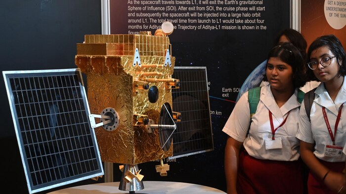 Des adolescentes vêtues d'un uniforme regardent la maquette d'une sonde spatiale. 