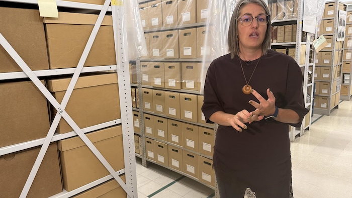 Joëlle Hardy devant des étagères où s'entassent des caisses d'archives.