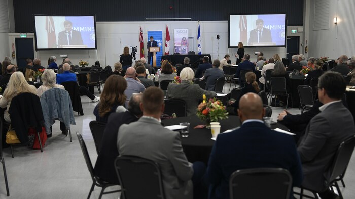 Plusieurs personnes assisses au tour des tables, devant un podium. 