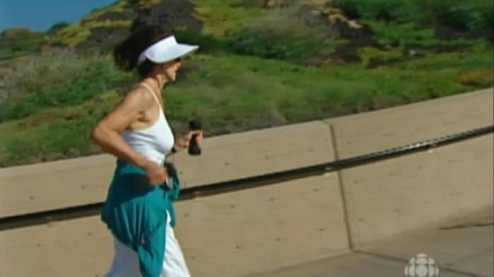 Femme qui fait de la course à pied en tenant de petits altères dans les mains. 