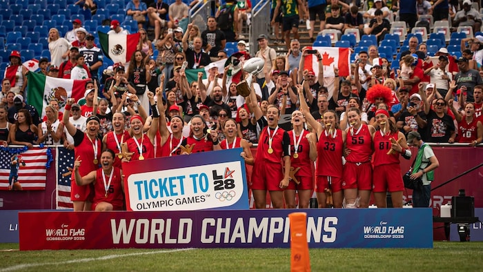 Les joueuses posent avec leur médaille d'or aux Mondiaux de football drapeau, une affiche « TICKET TO OLYMPIC GAMES LA28 » dans les mains.
