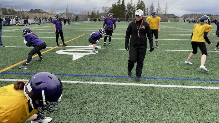 Une entraîneuse de football s'assure que ses joueuses effectuent bien un exercice. 