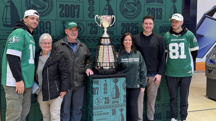 Les receveurs des Roughriders de la Saskatchewan, Dhel Duncan-Busby (à gauche), Mitchell Picton (à droite) et des partisans autour du trophée de la Coupe Grey.