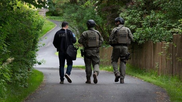 Trois membres de police de dos marchent dans une ruelle.