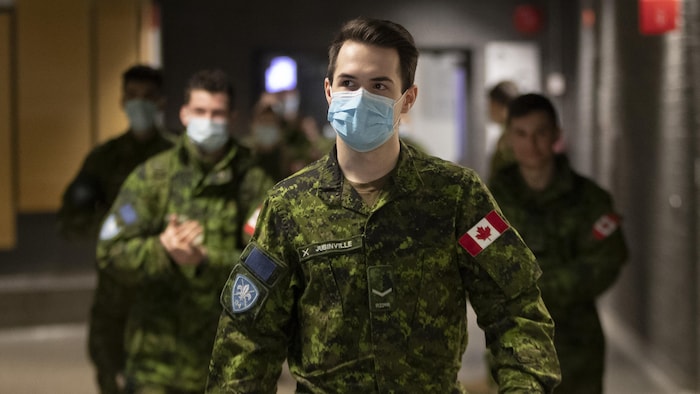 Des militaires des forces armées canadiennes, la plupart portant un masque, dans un couloir d'un collège.