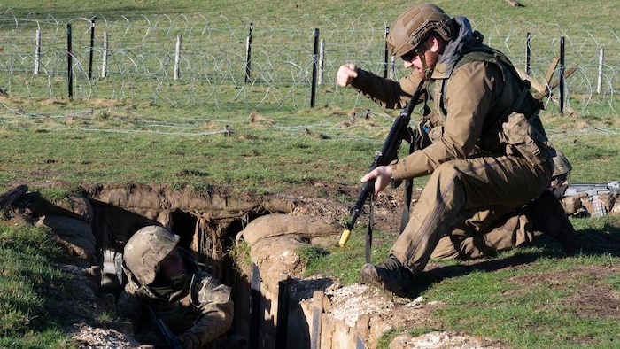 Un soldat dans une tranchée écoute un soldat qui lui donne des instructions.