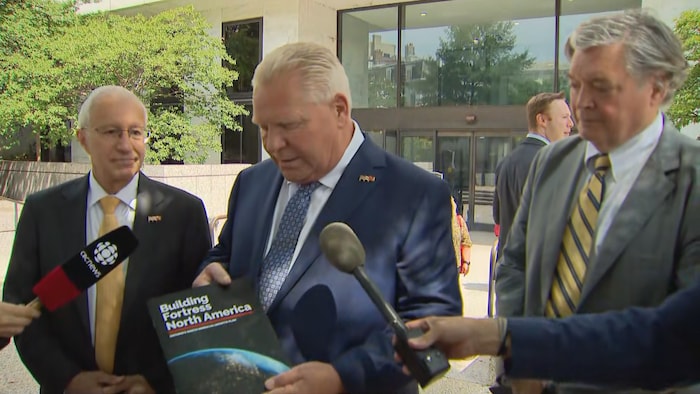 Doug Ford tient une brochure dans ses mains, où l’on peut lire les mots « Building Fortress North America » en anglais.