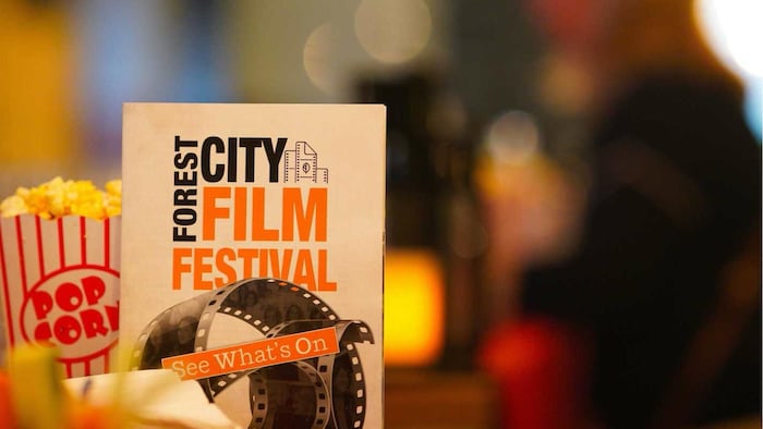Une brochure du Forest City Film Festival est exposée à côté d’un contenant de maïs soufflé, sur fond flou.