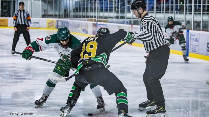 Deux hockeyeurs tentent de remporter la mise au jeu, alors qu'un juge de ligne vient de laisser la tomber la rondelle.