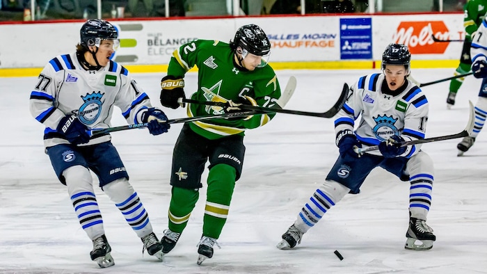 Un joueur des Foreurs, le capitaine Nathan Brisson, tente de passer entre deux joueurs des Saguenéens avec la rondelle.