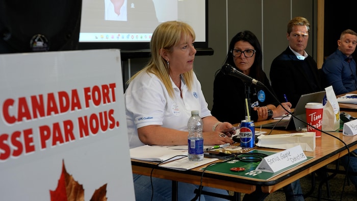 Plusieurs personnes assises à une table à côté d'une pancarte «Canada fort passe par nous».