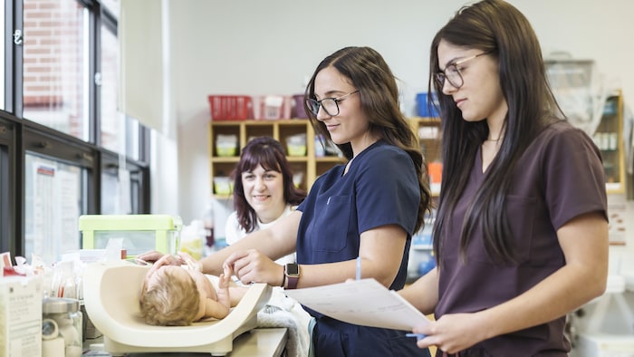Deux femmes infirmières en formation donnent des soins à un bébé sous le regard d'une autre femme.