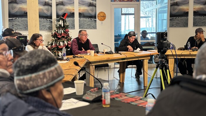 Des gens assis autour d'un longue table avec des micros à l'intérieur.