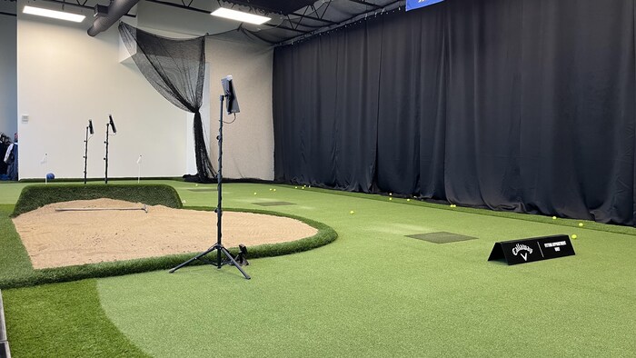 Une salle d'entraînement intérieure de golf avec une fosse de sable.