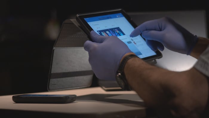 Les mains d'un douanier qui scrute un compte Facebook sur une tablette numérique.
