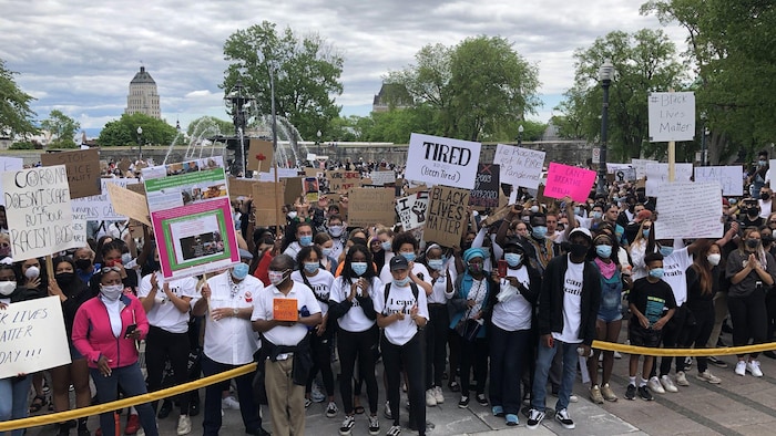 Une foule de manifestants tenant des pancartes devant l'Assemblée nationale.