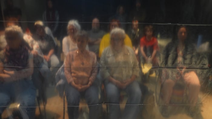 Plusieurs personnes sont assises dans une salle derrière des bâches.