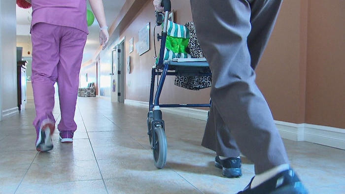 Une employée d'un foyer de soins et un homme poussant une marchette.