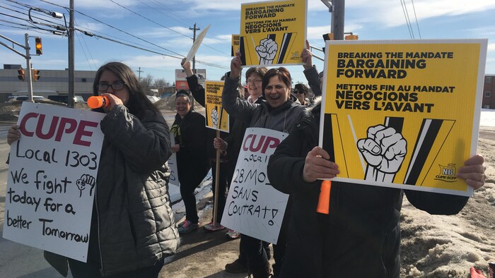 Une groupe de manifestants le long d'une rue à Moncton brandit des pancartes syndicales.