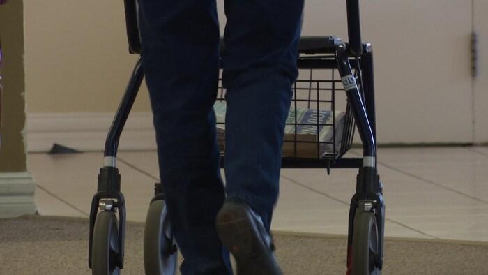 Les jambes et les pieds d'une personne qui avance avec l'aide d'une marchette.