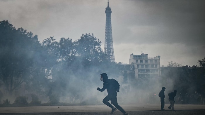 Un manifestant court lors d'une manifestation au milieu de la fumée des gaz lacrymogènes avec la tour Eiffel en arrière-plan.