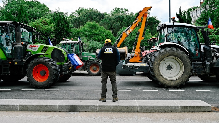 Un agriculteur observe plusieurs tracteurs garés sur la route devant la préfecture du Rhône, le 11 mai 2026.