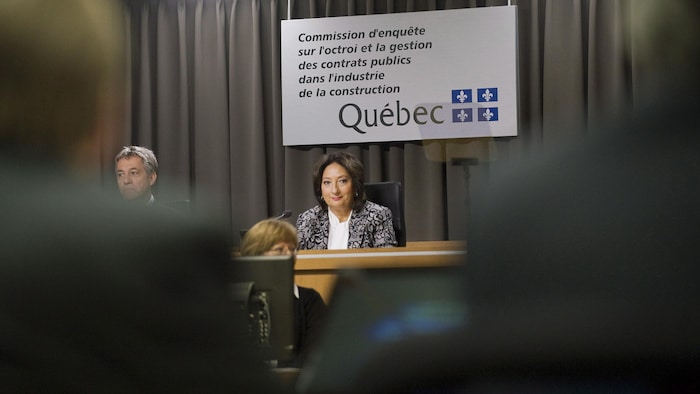La juge France Charbonneau assise à son bureau dans la salle d'audience de la commission. À ses côtés, le commissaire Renaud Lachance.
