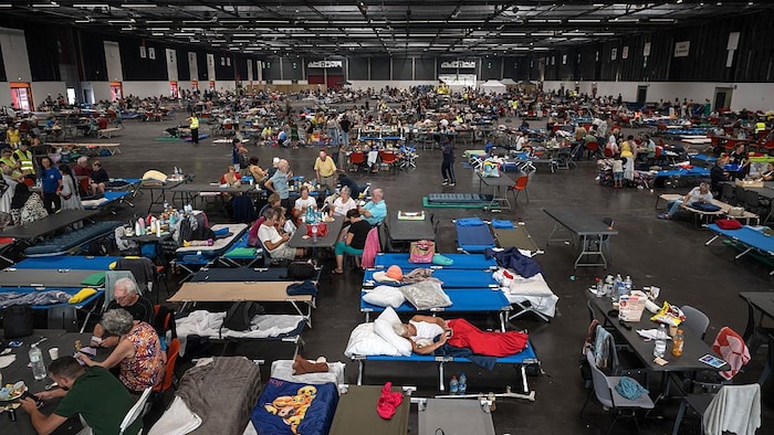 Des personnes étendues sur des lits ou couchées sur des chaises dans une grande salle.