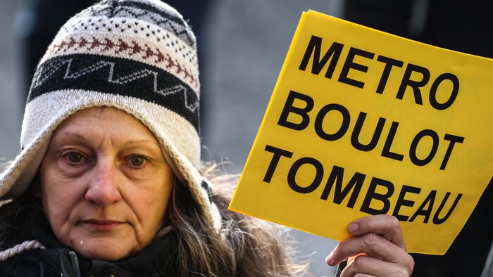Une manifestante tient un écriteau indiquant : « Métro, boulot, tombeau ».
