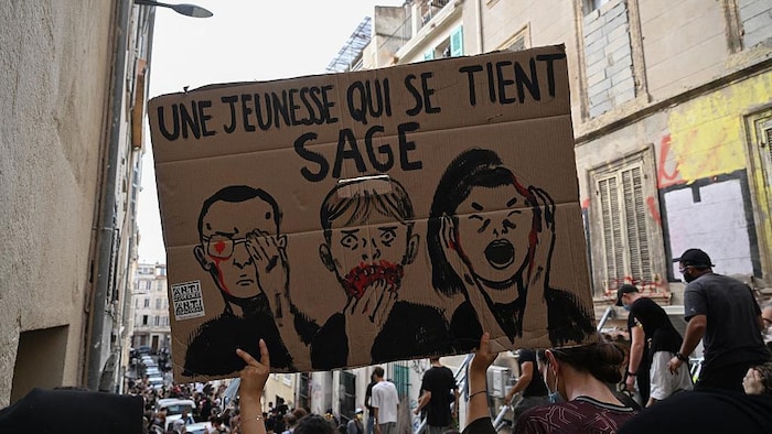 Un manifestant tient une pancarte sur laquelle on peut lire « Une jeunesse qui se tient bien » lors d’une manifestation d’élèves du secondaire.