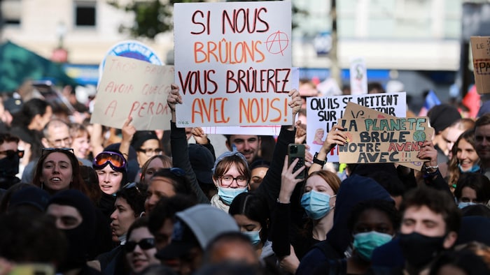Des manifestants brandissent des pancartes lors d’une manifestation, dont un où l'on peut lire : « Si on brûle, vous brûlerez avec nous ».
