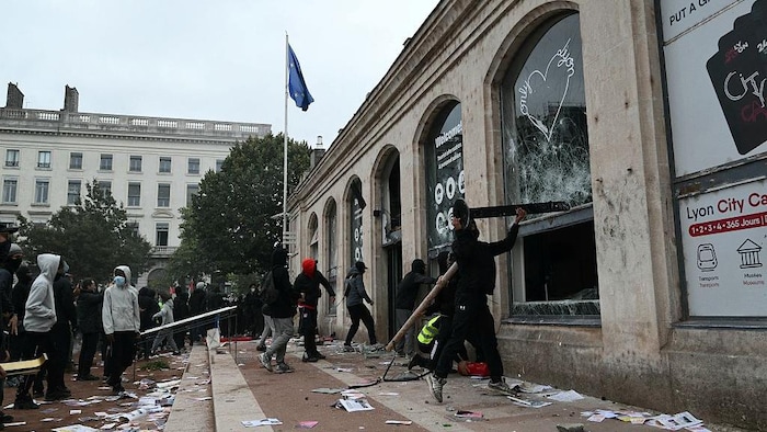 Des manifestants utilisent des barrières pour briser les vitres de l’office du tourisme de Lyon.