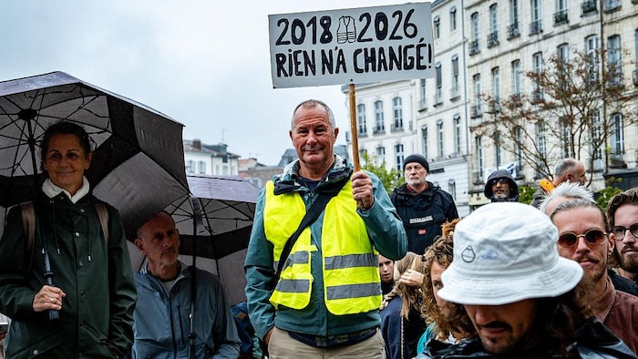 Un homme vêtu d’un chandail jaune et tenant une pancarte dénonçant l’absence de changement.