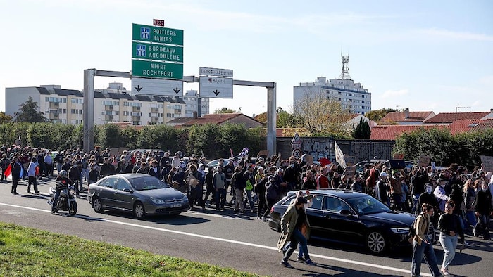 Des manifestants défilent tandis que des véhicules circulent sur la route.