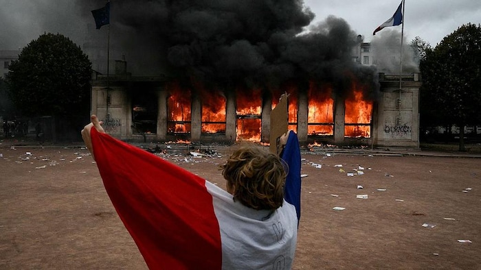 Un manifestant enveloppé dans un drapeau français se tient devant l'office du tourisme de Lyon incendié.