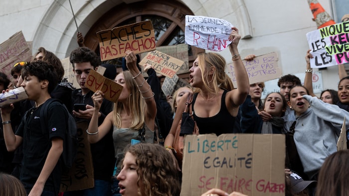 Des étudiants brandissent des pancartes devant un lycée.