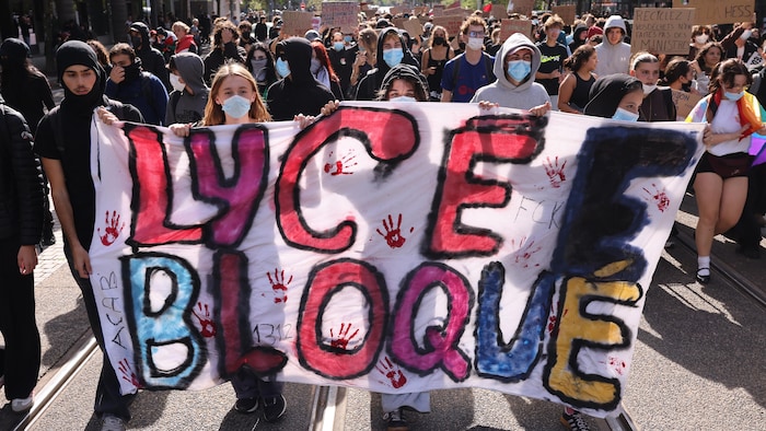 Des manifestants marchent dans la rue en tenant des pancartes.