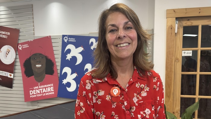 France Marion sourit à la caméra devant des affiches électorales de Québec solidaire épinglées sur un mur.