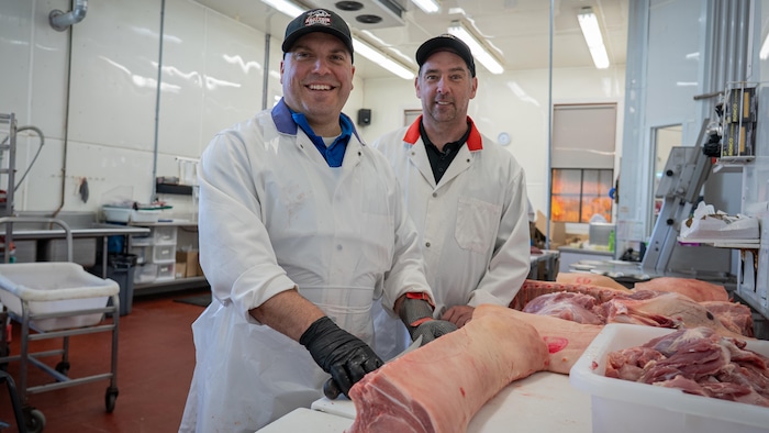Deux hommes derrière une longe de porc dans une boucherie.