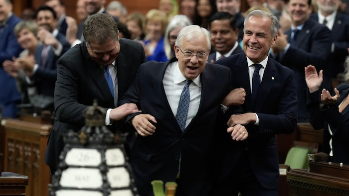 Mark Carney et Andrew Scheer conduisent Francis Scarpaleggia, dans la bonne humeur et sous les applaudissements des députés, à son siège de président de la Chambre, feignant de le contraindre.