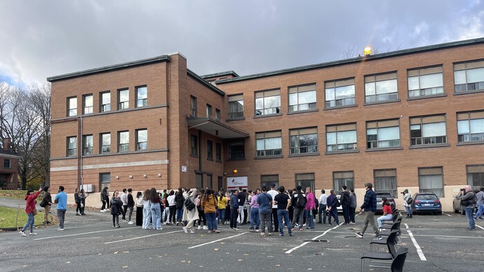 Des dizaines d'étudiants sont rassemblés à l'extérieur, sur le terrain d'une école.