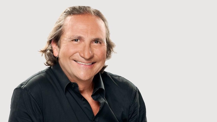 Franco Nuovo souriant et portant une chemise noire échancrée.