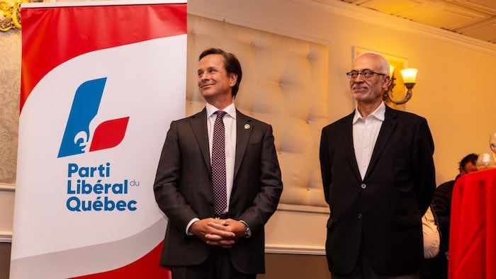 Frédéric Beauchemin se tient debout au côté de Carlos Leitao devant une bannière du Parti libéral du Québec.