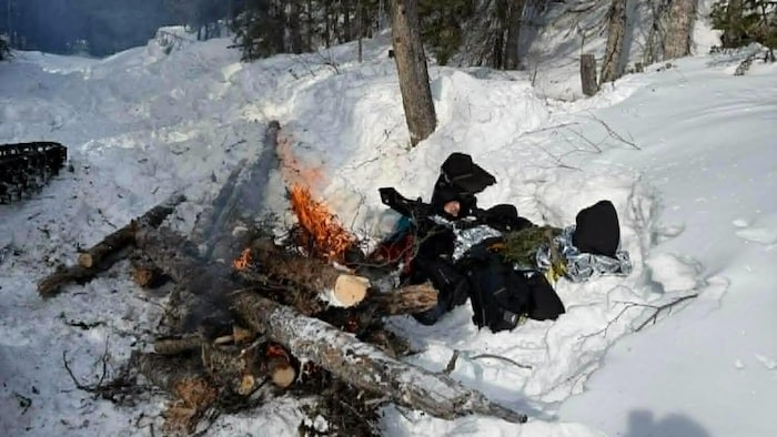François Champagne est couché dans la neige, à proximité d'un grand feu. 