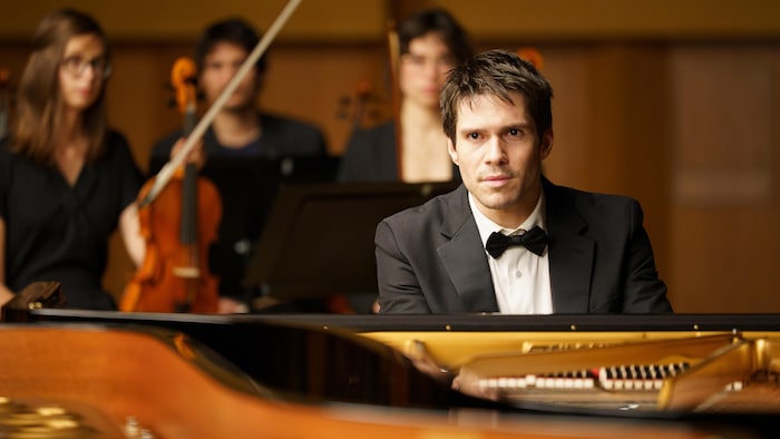 Un representation    de François Civil derrière un piano.