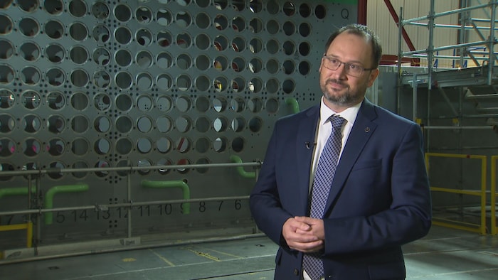 M. Cussac regarde devant lui. Il se tient debout devant la maquette de réacteur nucléaire grandeur quality de Darlington.