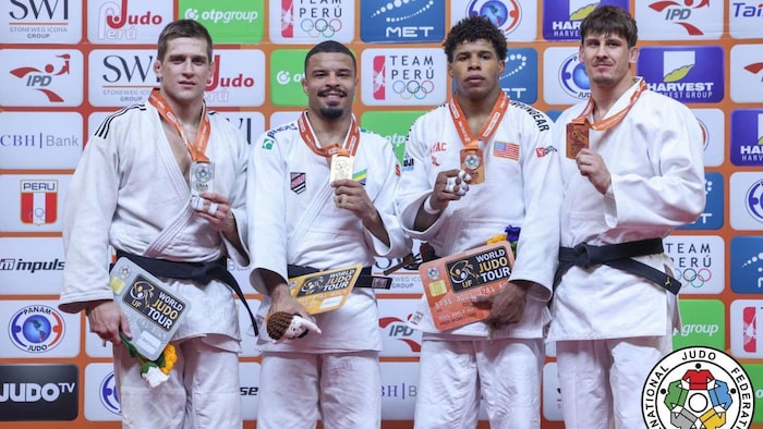 Quatre judokas masculins en kimono blanc se tiennent côte à côte sur un podium de compétition devant un mur sponsorisé.