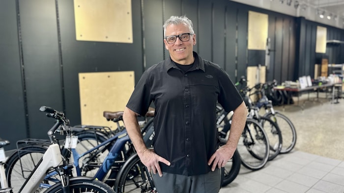 Un homme de bout se fait prendre en photo au milieu de vélos. 