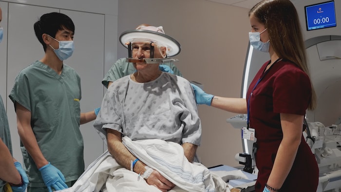 Un homme sur une civière en jaquette d'hôpital avec un disque autour de la tête. 